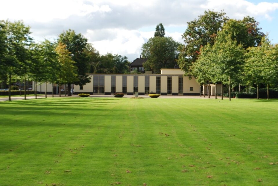 Het karakteristieke aulagebouw van de Noorderbegraafplaats in Hilversum, gezien vanaf het groene grasveld.