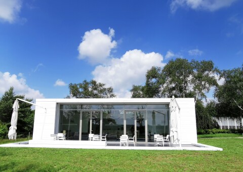 Buitenzijde van De Einder op Zuiderhof met een glazen gevel, witte constructie en groen gazon.