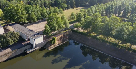 Luchtfoto van een gebouw tussen bomen, aan een waterpartij.
